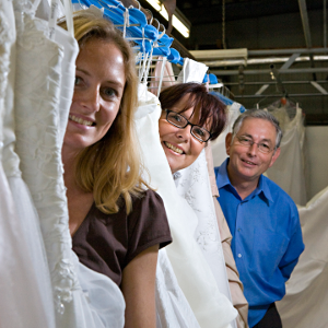 Yvonne, Ursula und Axel Herbrand lächelnd zwichen gereinigten Brautkleidern